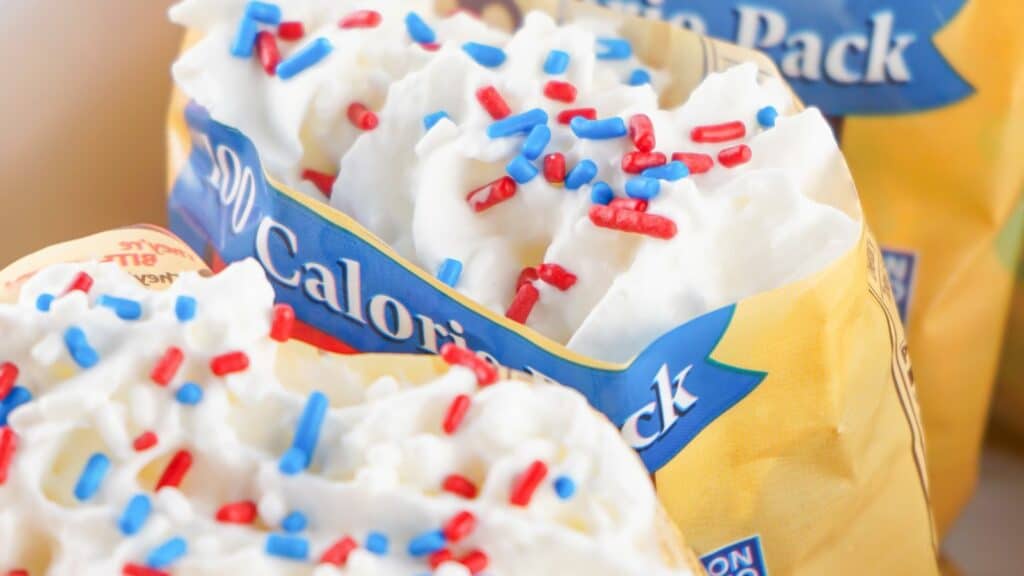 Close-up image of a snack pack filled with whipped cream topped with red, white, and blue sugar sprinkles. Packaging displays "90 Calorie Pack." The festive colors make this treat perfect for a patriotic gathering or as an addition to your walking pretzel salad.