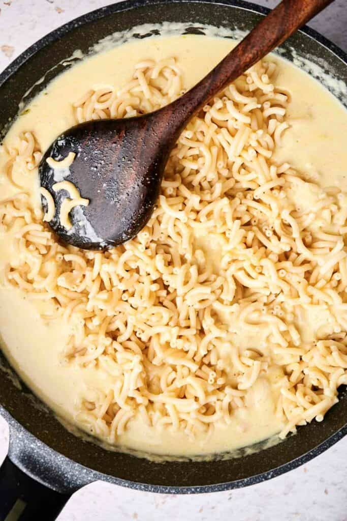 A skillet filled with creamy mac and cheese, with perfectly cooked macaroni pasta bathed in a rich cheese sauce. A wooden spoon rests on top of the delectable dish.
