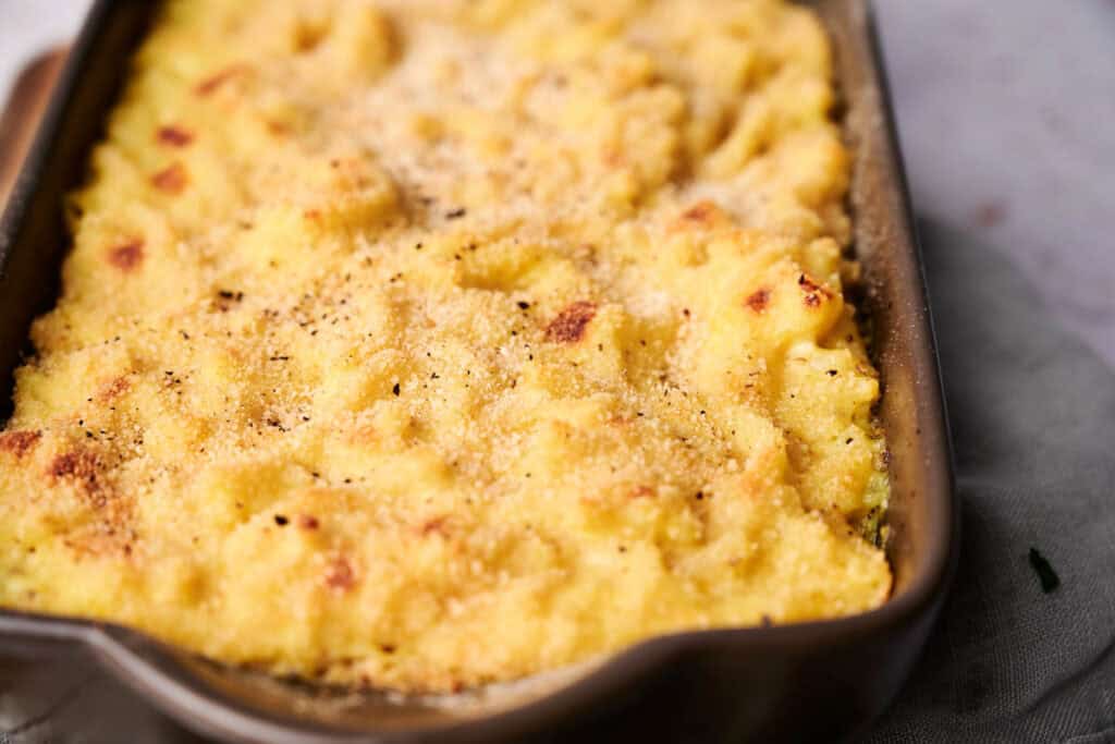 A close-up of a baked mac and cheese featuring a golden-brown topping beneath the surface.
