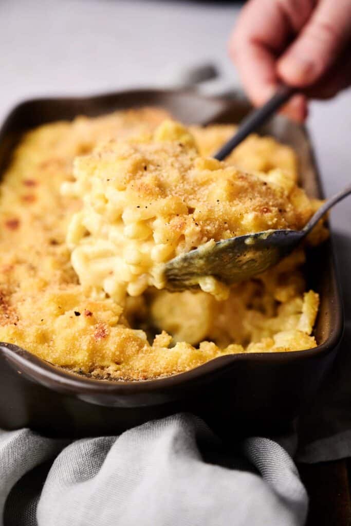 A close-up of a baking dish with golden-brown mac and cheese being scooped out with a large spoon.