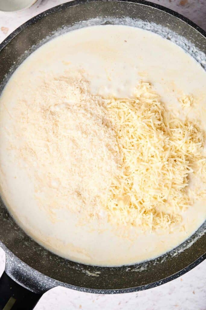 A skillet filled with creamy white sauce and shredded cheese being stirred together, creating the perfect mac and cheese.