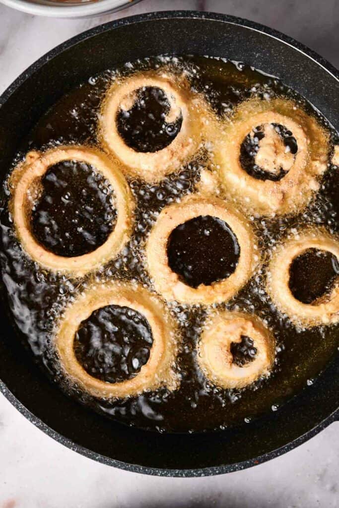 Golden brown onion rings sizzling to perfection in hot oil within a black pan.