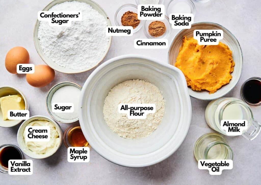 A selection of labeled baking ingredients, including all-purpose flour, pumpkin puree, eggs, sugar, butter, cream cheese, spices, and liquids&mdash;plus a bowl of colorful Patriotic Gumdrops&mdash;arranged on a countertop.