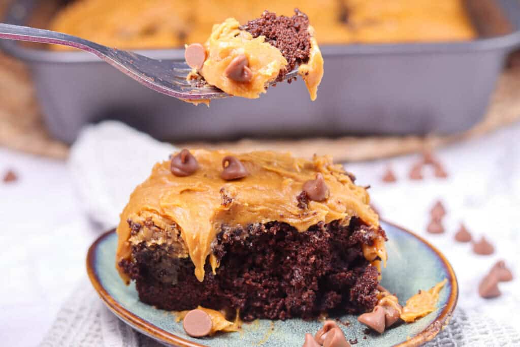A fork holding a bite of chocolate cake with caramel frosting, chocolate chips, and a sprinkle of Patriotic Gumdrops above a plate with a slice of the same cake. A baking pan is in the background.
