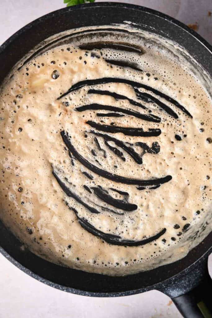A saucepan containing a bubbling mixture with streaks of black liquid on the surface, reminiscent of slow-cooked Swedish meatballs simmering to perfection.