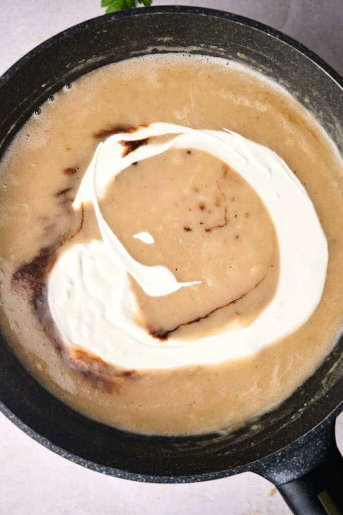 A pot containing a creamy sauce with a swirl of what appears to be cream or yogurt on its surface, perfect for drizzling over Swedish meatballs.
