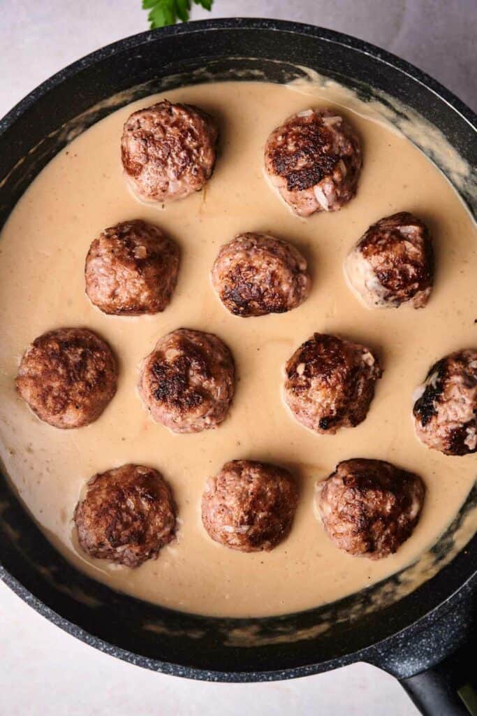 A black skillet containing several browned Swedish meatballs in creamy sauce.