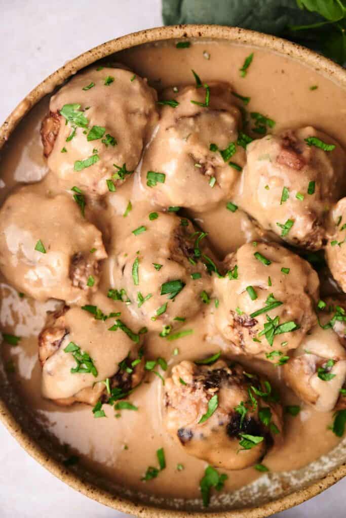 A bowl of Swedish meatballs covered in creamy sauce and garnished with chopped fresh herbs.