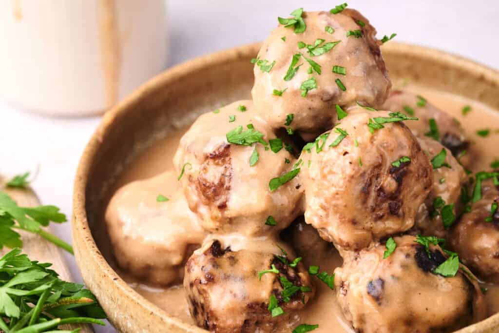 A bowl of Swedish meatballs covered in creamy sauce, garnished with chopped parsley.