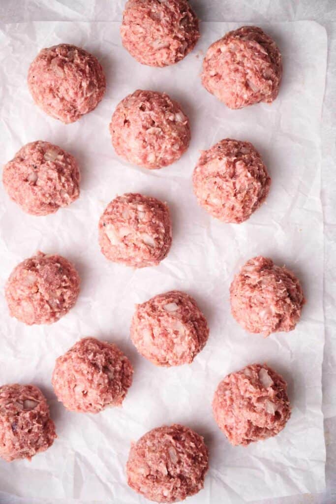 Thirteen raw Swedish meatballs are arranged on a sheet of parchment paper.