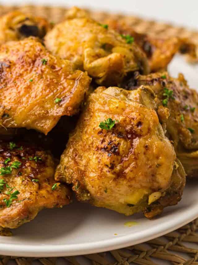 A plate of roasted chicken thighs garnished with chopped herbs, resting on a woven placemat.