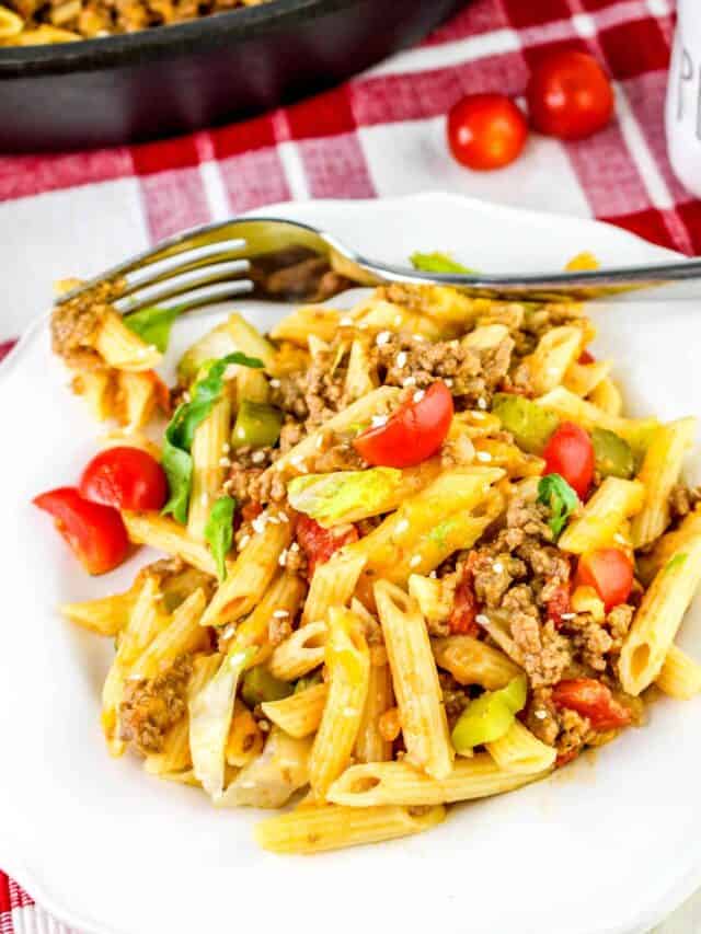 A plate of penne pasta mixed with ground meat, sliced cherry tomatoes, bell peppers, and garnished with herbs. A fork rests on the plate. The background includes a red-and-white checkered cloth.