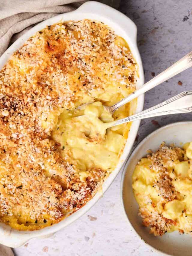 A baking dish filled with baked macaroni and cheese with a crispy breadcrumb topping. A portion is served in a small bowl with two forks.