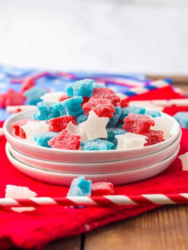 A bowl filled with red, white, and blue star-shaped gummy candies on a red cloth, accompanied by striped straws.