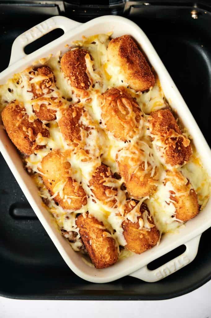         A baked dish of breaded and fried croquettes topped with melted cheese in a white rectangular baking dish, reminiscent of an air fryer tater tot casserole.