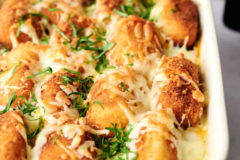A close-up of a casserole dish filled with baked golden brown breaded chicken breasts, topped with melted cheese and garnished with chopped fresh herbs, reminiscent of an air fryer tater tot casserole.