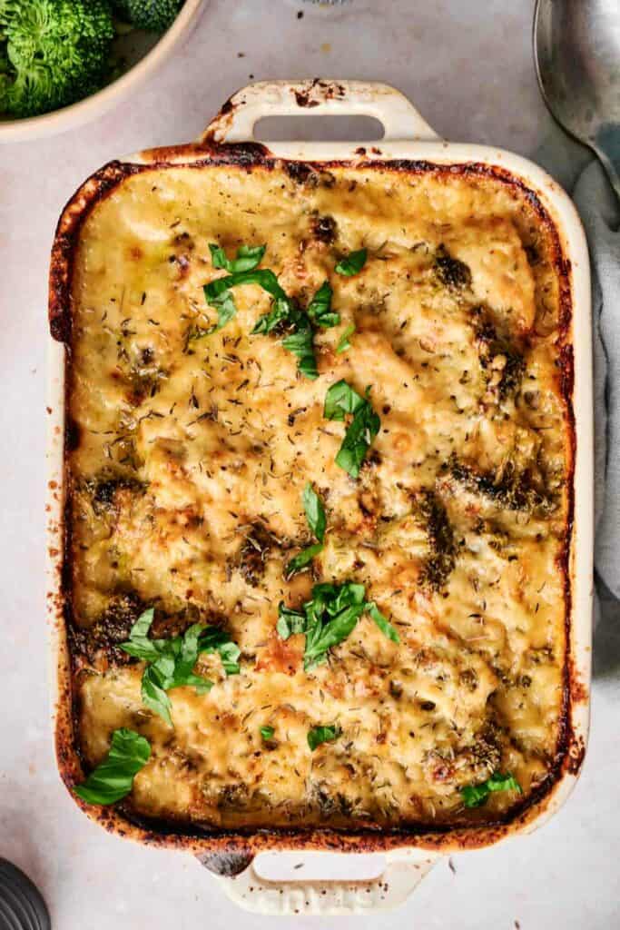 A baked chicken and broccoli casserole dish filled with a cheesy, golden-brown bake, garnished with fresh herbs.