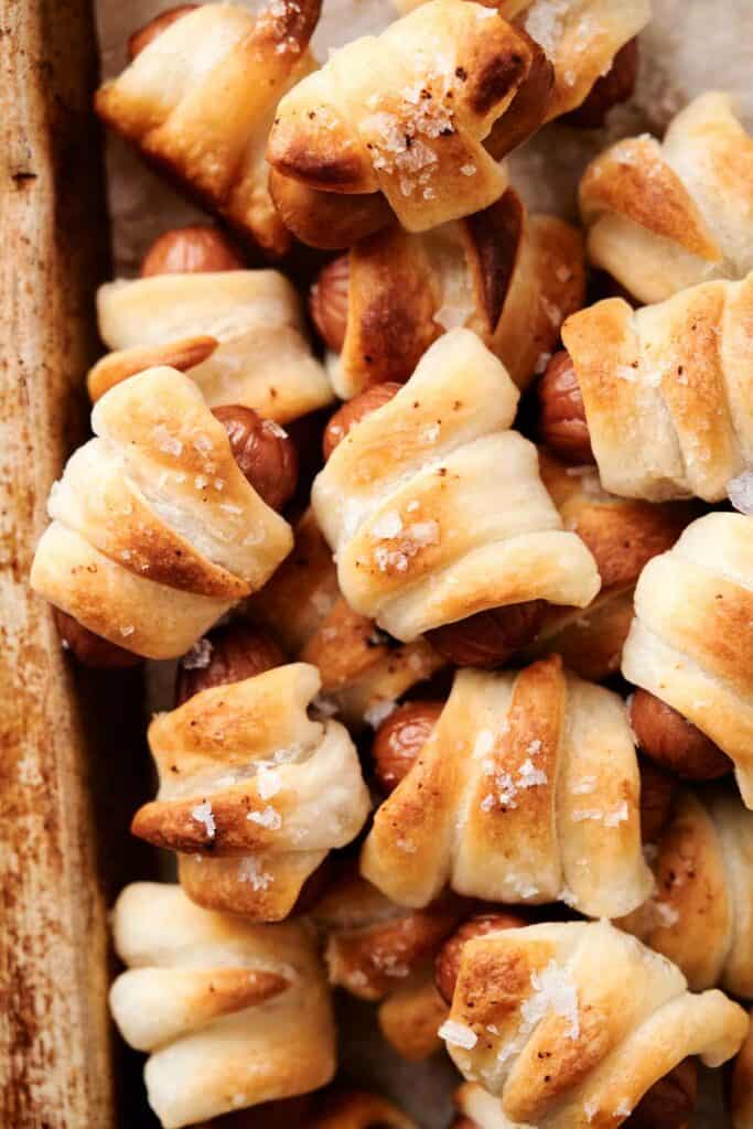 A close-up view of golden-brown mini sausages wrapped in puff pastry, topped with a sprinkle of coarse salt, on a baking sheet - the perfect air fryer pigs in a blanket.