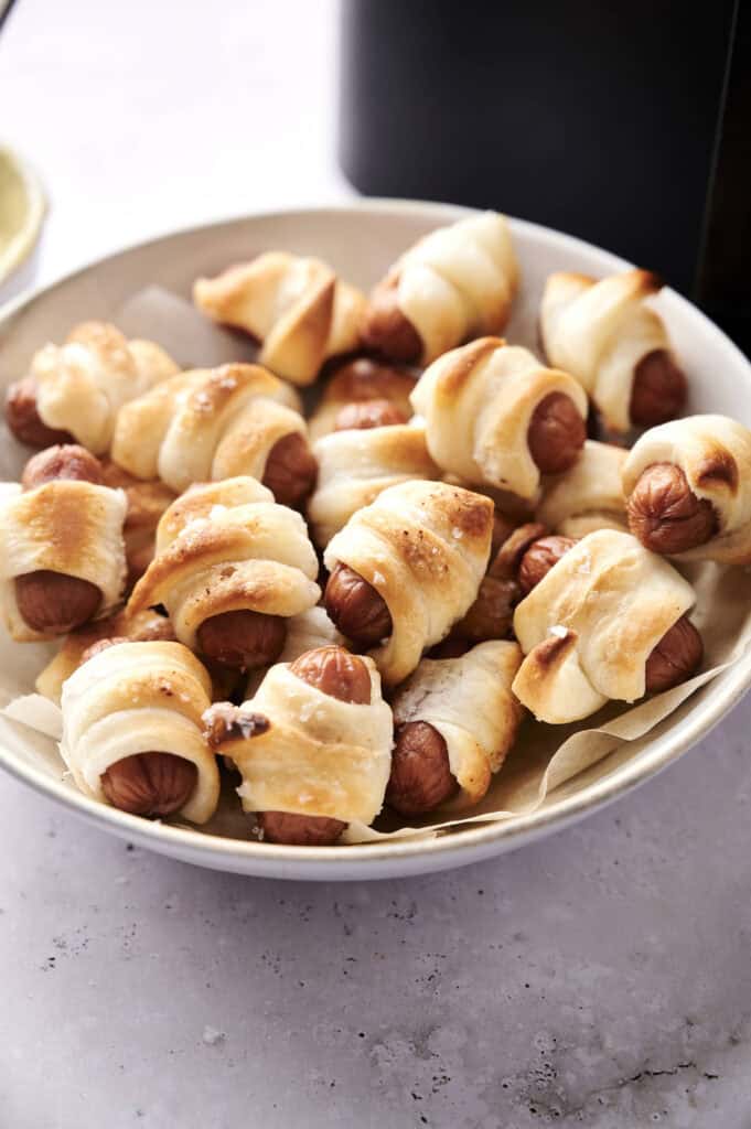 A white bowl filled with delicious air fryer pigs in a blanket — small sausages wrapped in puff pastry and perfectly crisped.