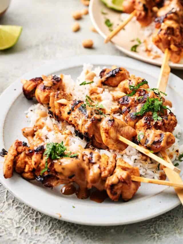 Grilled chicken skewers on a bed of white rice, drizzled with sauce and garnished with chopped herbs, served on a white plate.