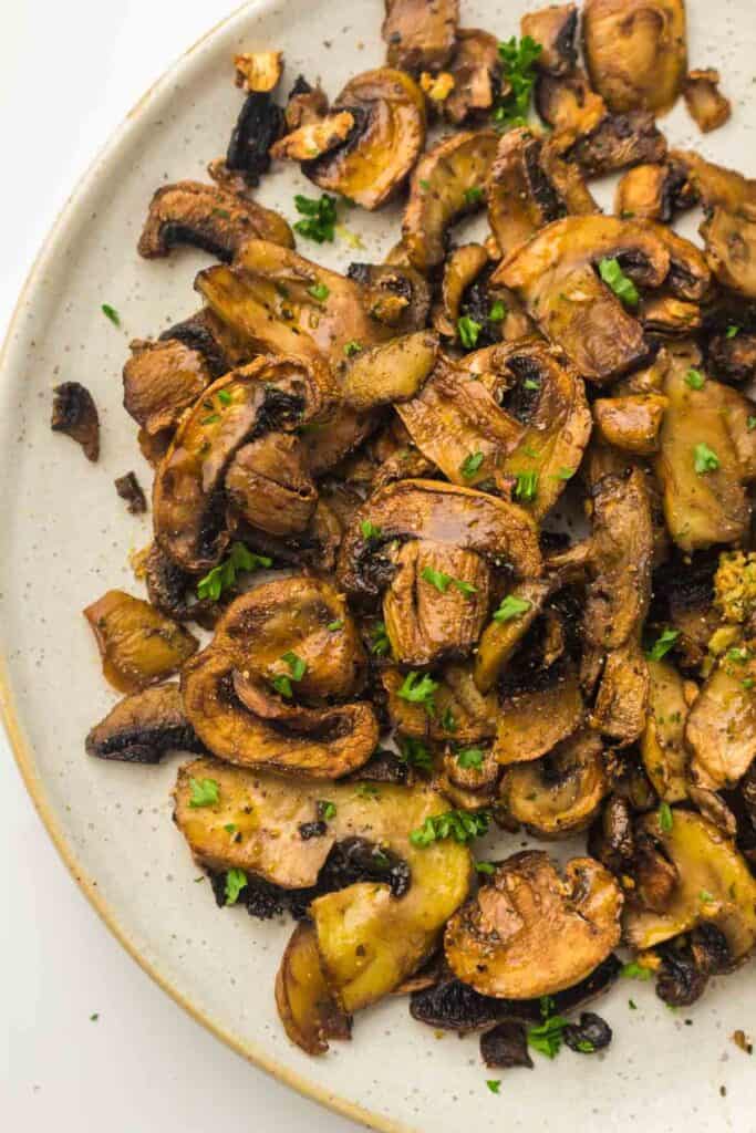 A plate of air fryer mushrooms, perfectly sautéed and garnished with chopped parsley.