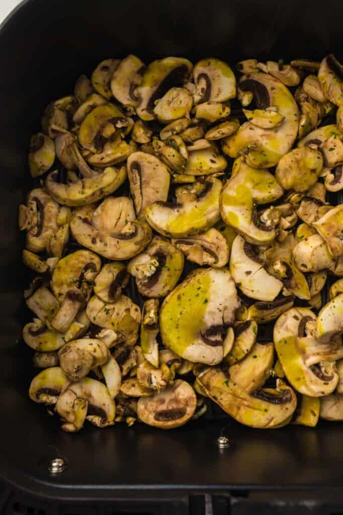 A container filled with air fryer mushrooms, seasoned with herbs and yellowish oil.