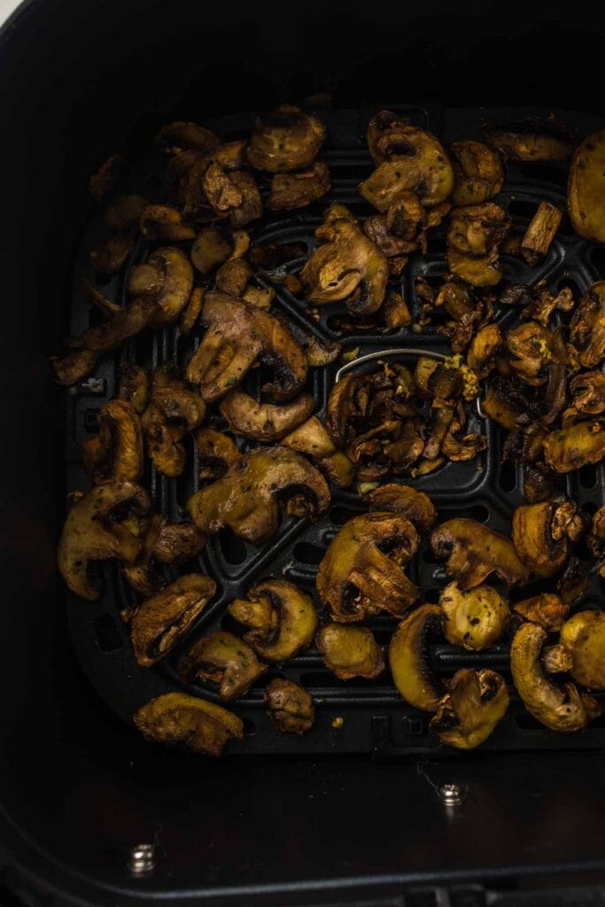 Air fryer mushrooms, seasoned and air fried to perfection, are beautifully arranged on a black air fryer basket tray.