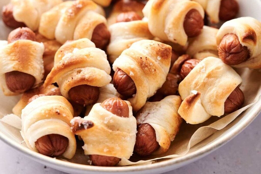 A bowl filled with air fryer pigs in a blanket, featuring small sausages wrapped in golden-brown pastry dough for a perfectly crisp bite.