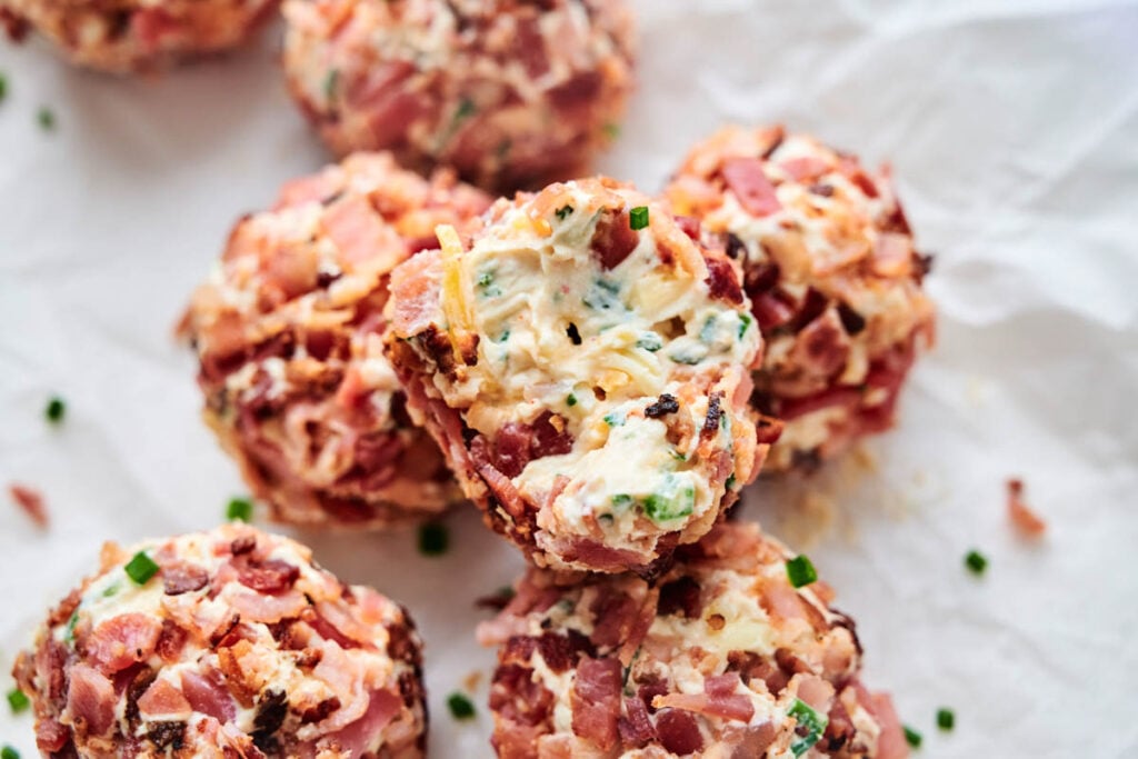Close-up of Bacon Jalapeno Popper Cheese Balls with herbs, placed on white parchment paper, showing a creamy filling and garnished with chives.