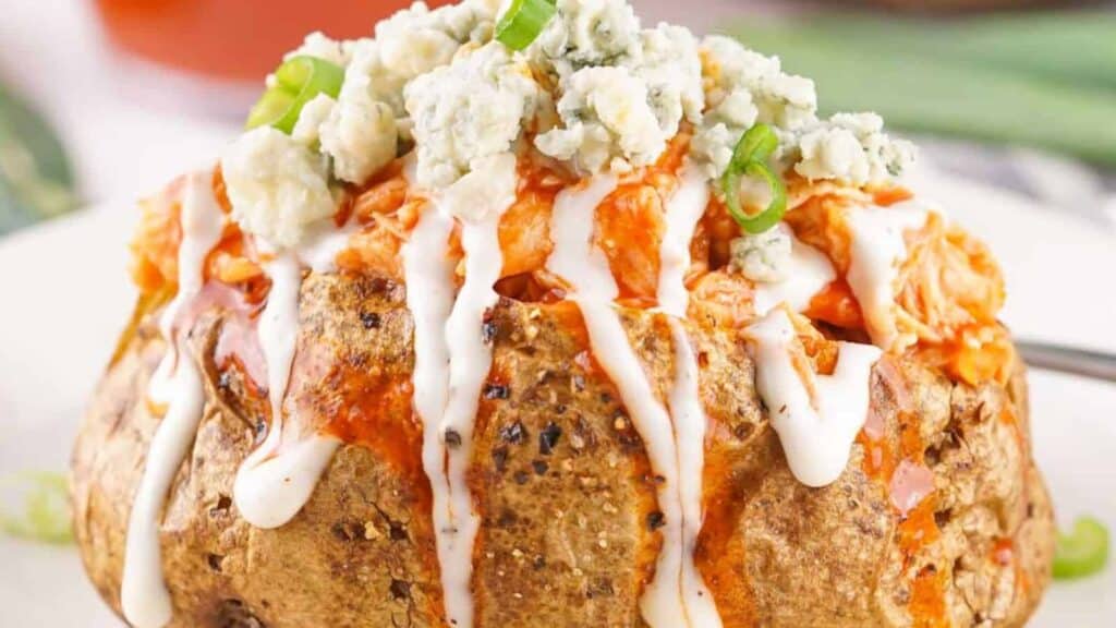 A baked potato topped with buffalo chicken, blue cheese crumbles, chopped green onions, and drizzled with ranch and buffalo sauce.