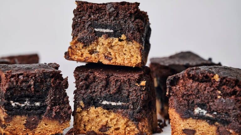 Stacked dessert bars featuring layers of chocolate brownie, a cookie center, and a cookie dough base, arranged on a plain white background.