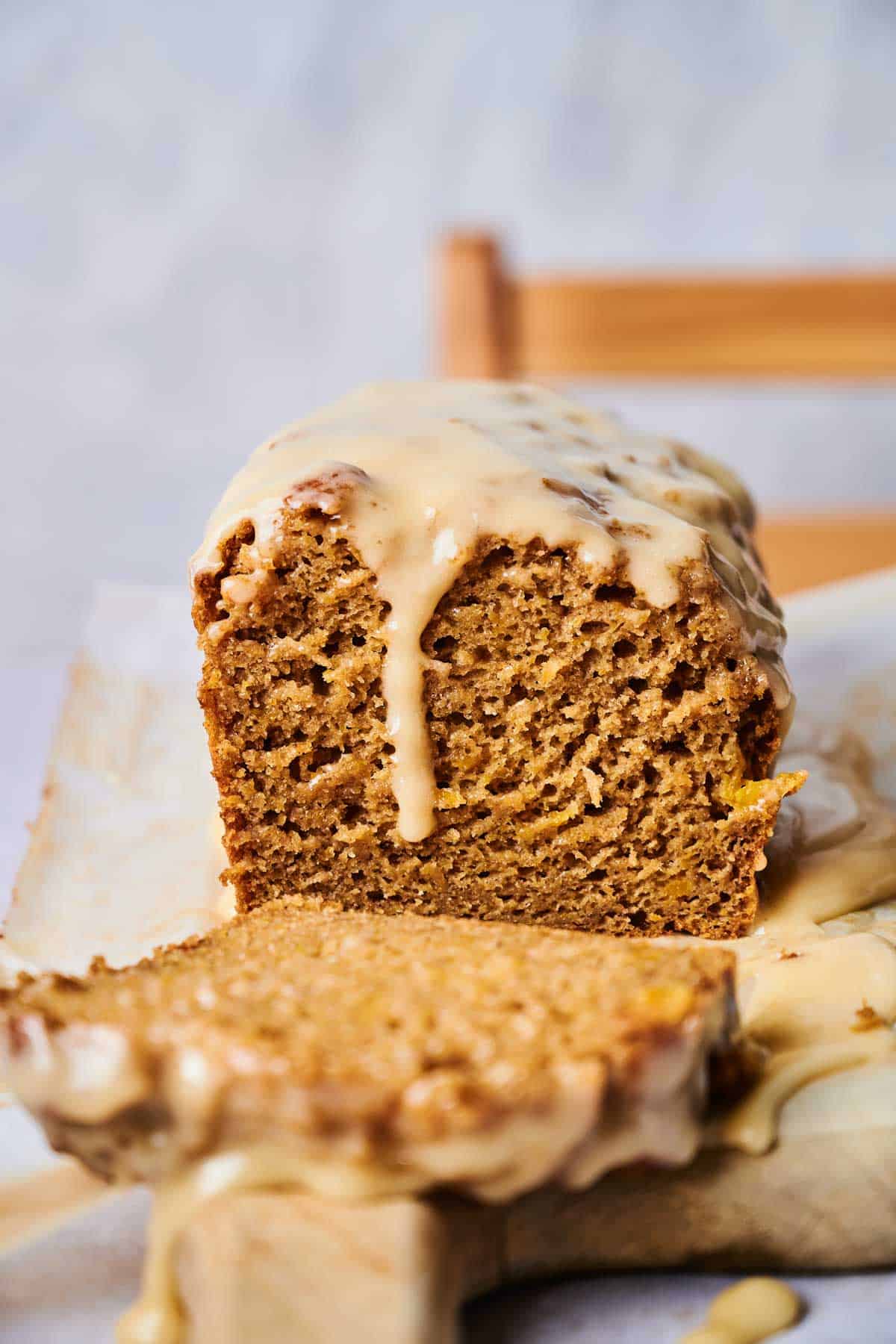 A loaf of pumpkin bread, partially sliced, topped with a thick glaze, on parchment paper with a blurred background.