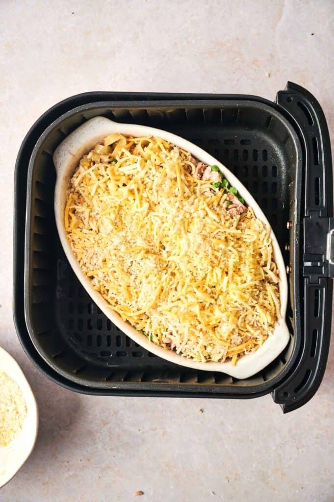 Oval ceramic dish filled with shredded cheese and breadcrumbs inside an air fryer basket.