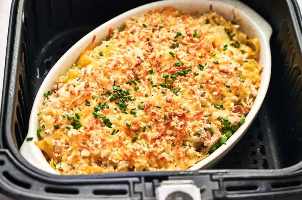 A baked pasta dish with a golden breadcrumb topping and finely chopped green herbs is placed in an air fryer.
