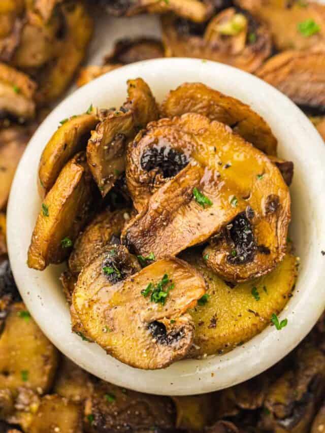 Close-up of sautéed mushrooms garnished with parsley in a white bowl.