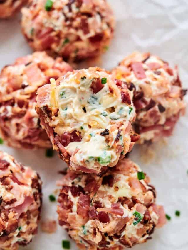 Close-up of several bacon cheddar ranch cheese balls garnished with herbs on a white crumpled paper background.