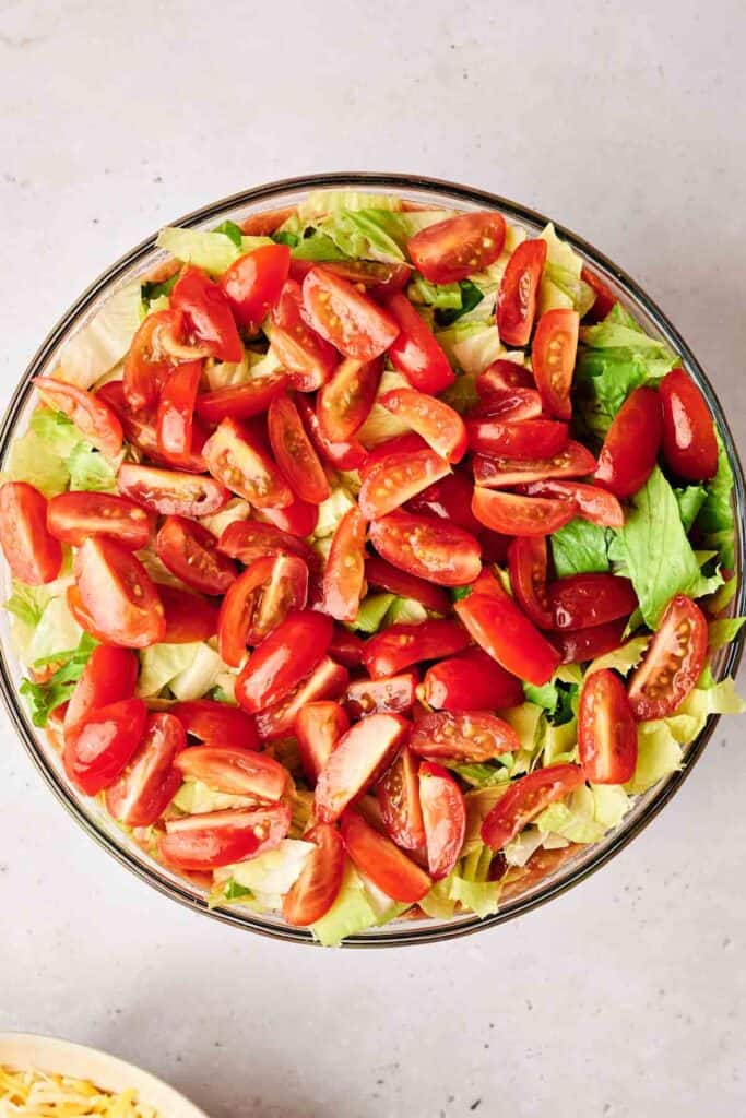 A bowl of salad with chopped lettuce and halved cherry tomatoes on a light-colored surface, reminiscent of the vibrant layers found in a 7 Layer Dip.