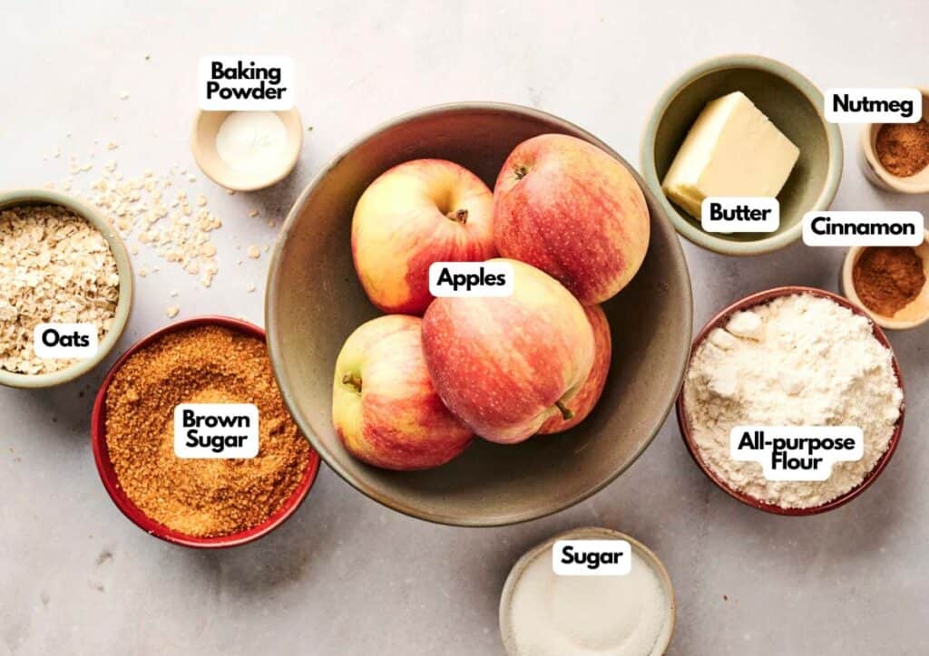 Top view of bowls containing apples, butter, flour, oats, brown sugar, sugar, baking powder, cinnamon, and nutmeg, each labeled with text.