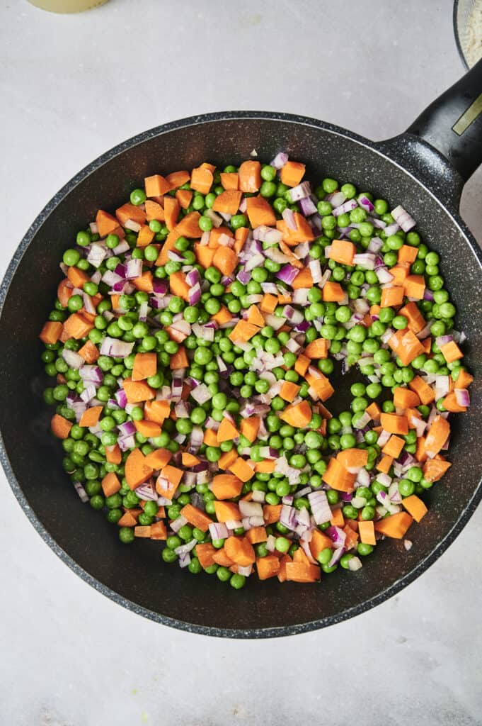 A frying pan filled with a mixture of diced purple onions, peas, and cubed sweet potatoes evokes the hearty comfort of a chicken and dumpling casserole.