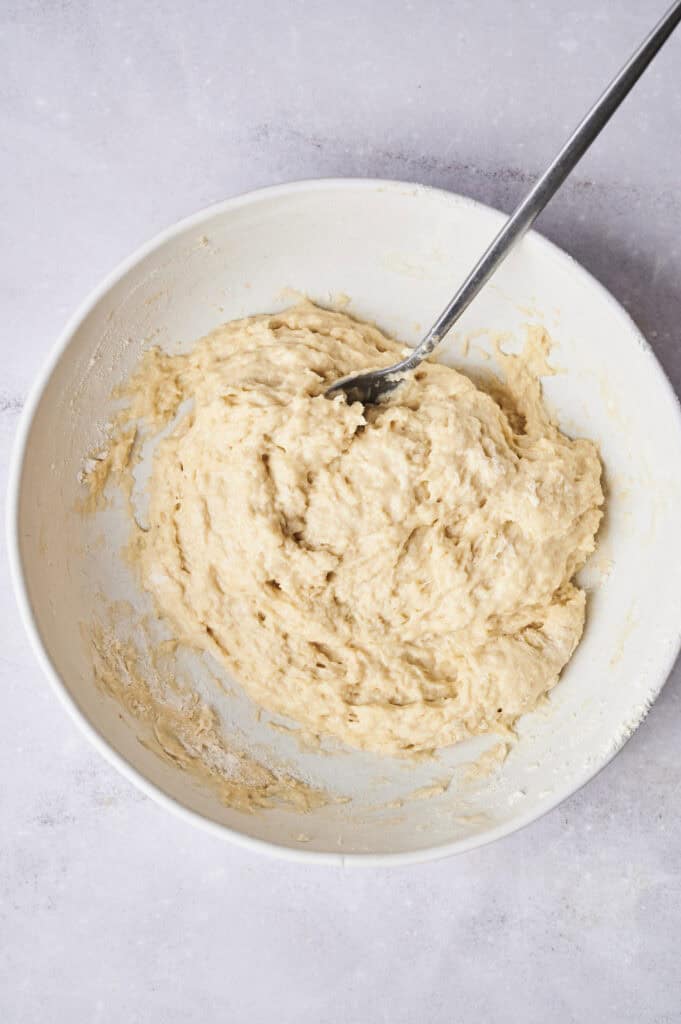 A bowl containing thick, beige dough with a spoon sticking out, reminiscent of the comforting base for a chicken and dumpling casserole.