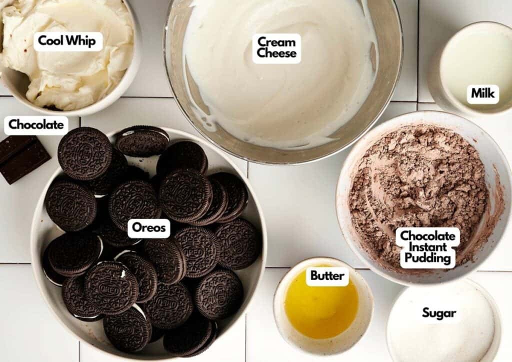Overhead view of Chocolate Lasagna ingredients in bowls on a white surface: Cool Whip, cream cheese, milk, chocolate, Oreos, chocolate instant pudding, butter, and sugar.