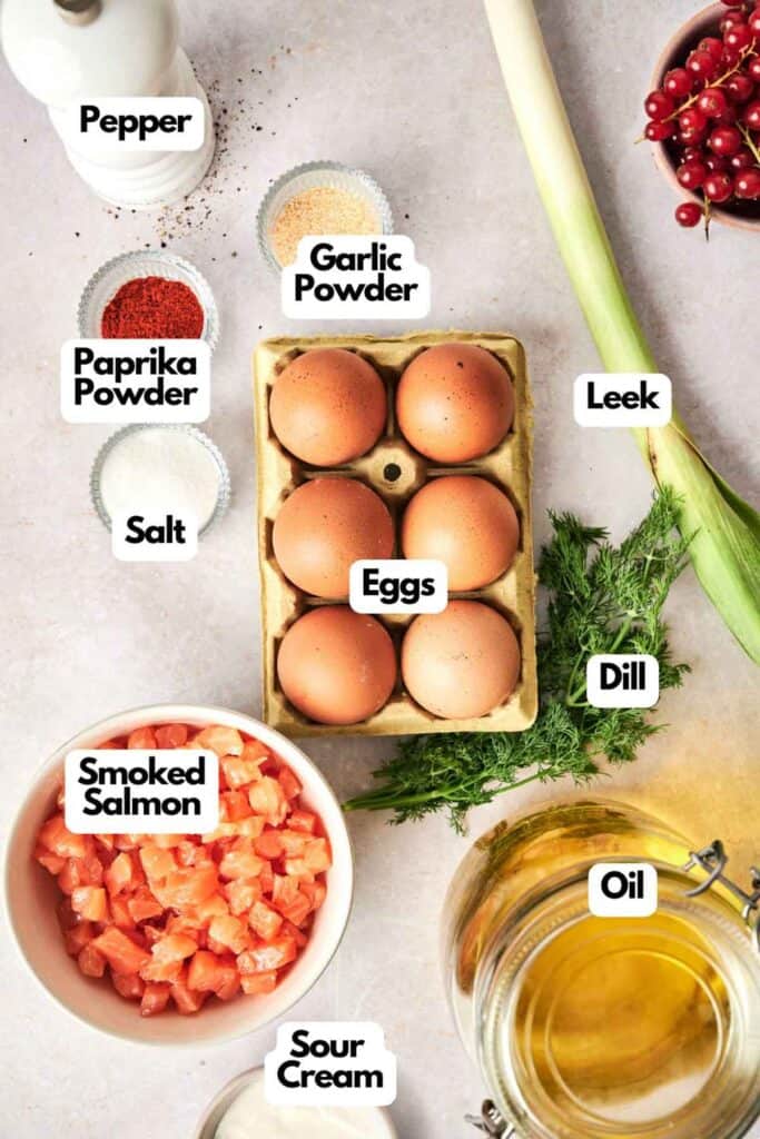 Ingredients laid out on a table: pepper, paprika powder, salt, garlic powder, leek, dill, oil, smoked salmon, sour cream, eggs in a carton ready for deviled eggs, and cranberries.