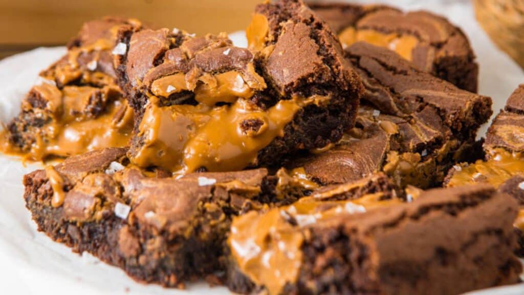 A close-up of caramel-filled brownies, showing a gooey caramel center and flaky sea salt sprinkled on top.
