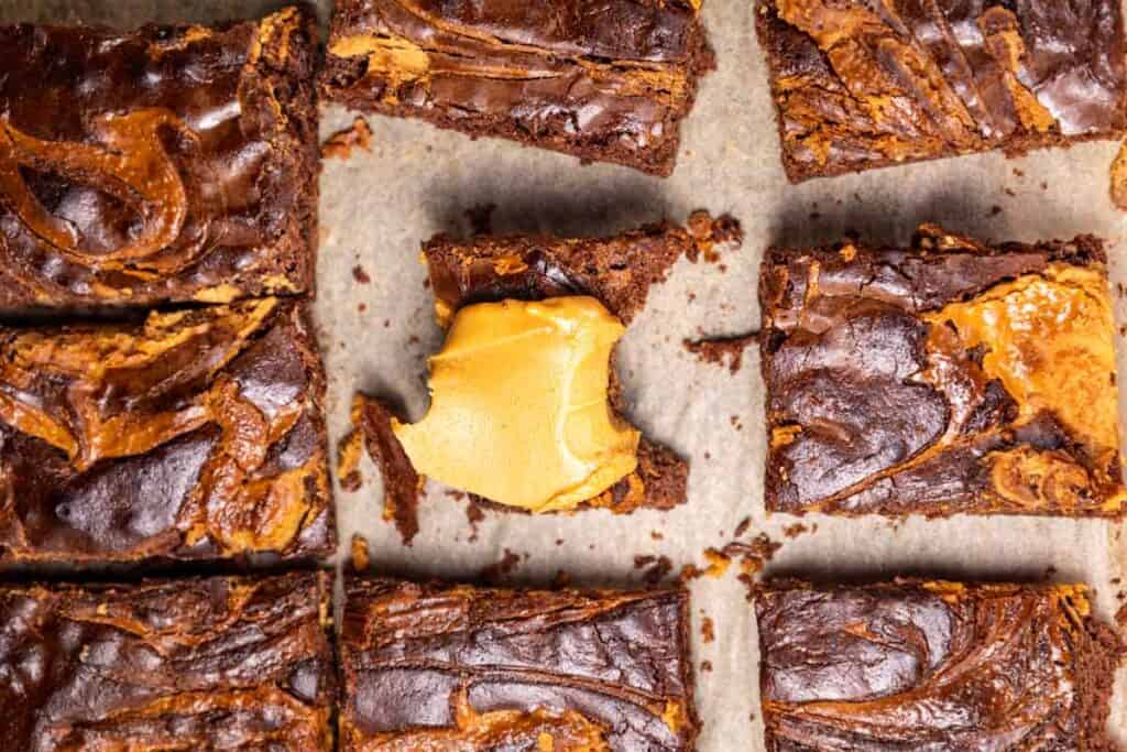 Nine Chocolate Pumpkin Patch Brownie Cake squares with swirled peanut butter on top, one missing a corner, arranged on parchment paper.
