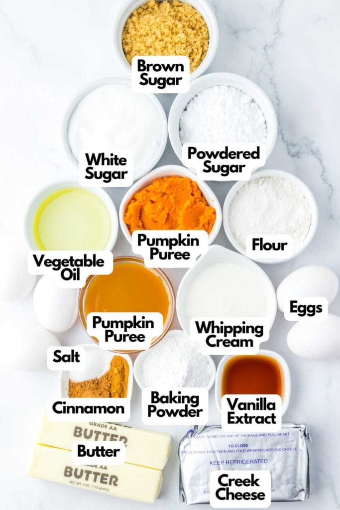 Assorted baking ingredients arranged in a pyramid shape, including brown sugar, white sugar, powdered sugar, vegetable oil, pumpkin puree for a delightful Pumpkin Caramel Cake, flour, eggs, salt, cinnamon, baking powder, vanilla extract, butter, and cream cheese.
