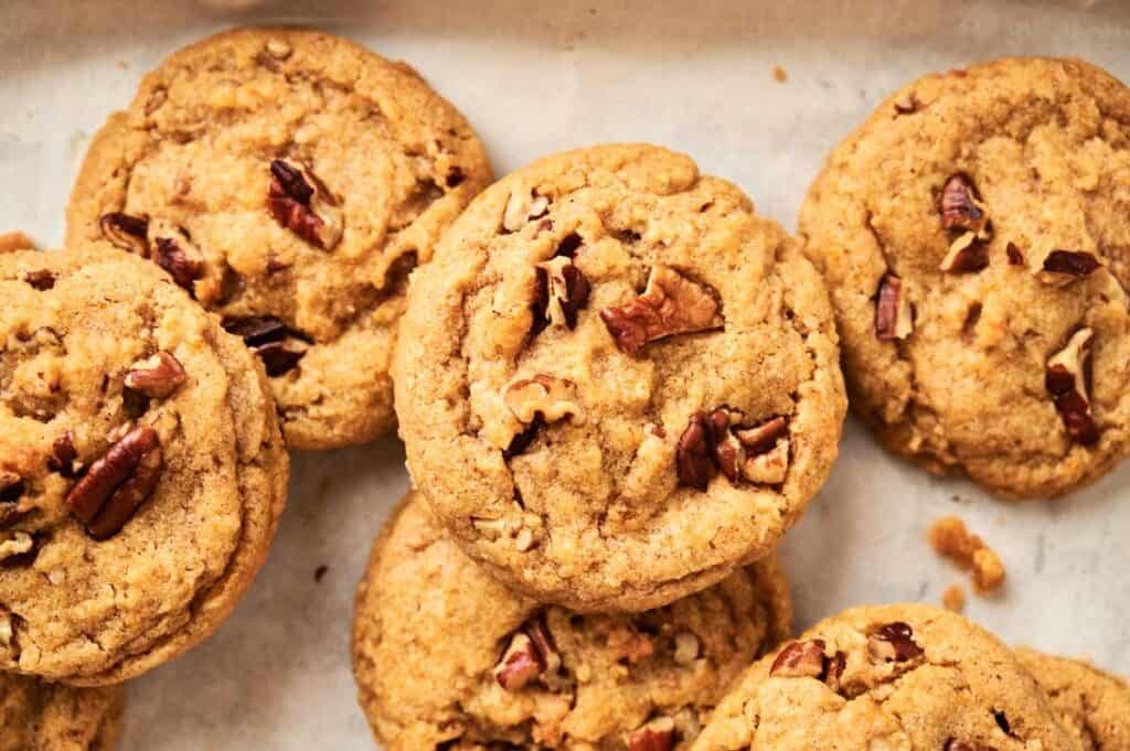 A close-up of several Pumpkin Cookies With Pecans on parchment paper, showcasing their golden-brown color and generous chunks of pecans on top.