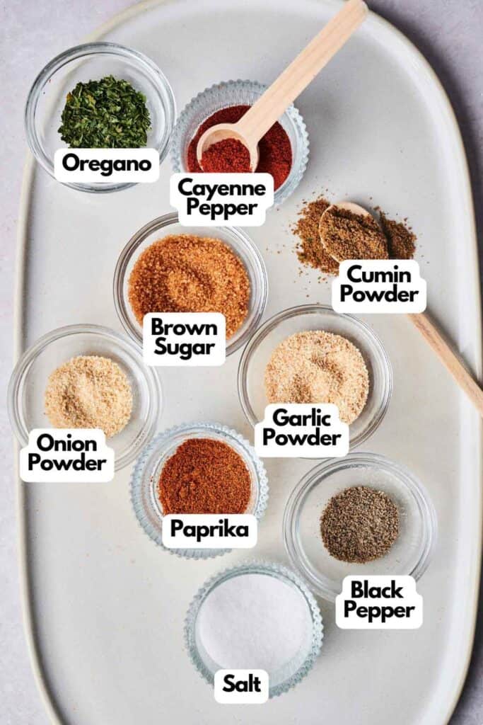 Nine small bowls of spices, including Oregano, Cayenne Pepper, and Cumin Powder, arranged on a white tray. The selection could perfectly capture the essence of a Wingstop Louisiana Rub with a hint of Brown Sugar, Onion Powder, Garlic Powder, Paprika, Black Pepper, and Salt.