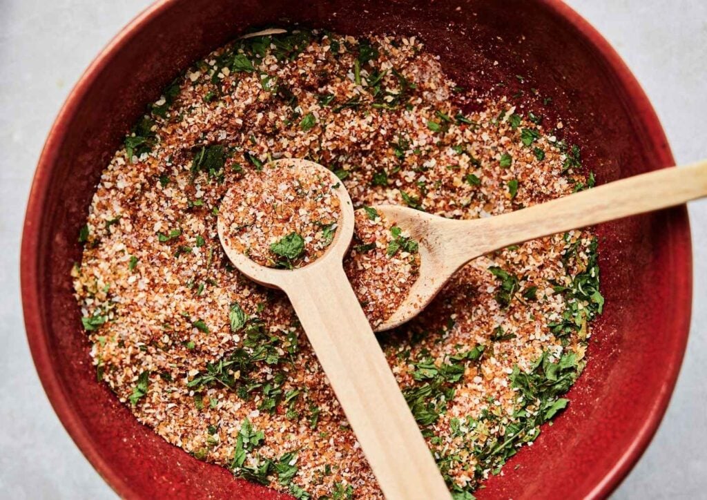 Red bowl of homemade Wingstop Louisiana rub spice blend with two wooden spoons, one holding a small scoop of the mixture.