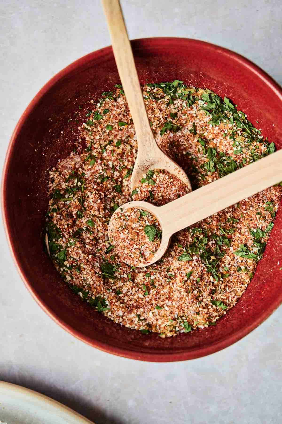 A red bowl containing a Wingstop Louisiana Rub seasoning blend, with two wooden spoons resting inside.