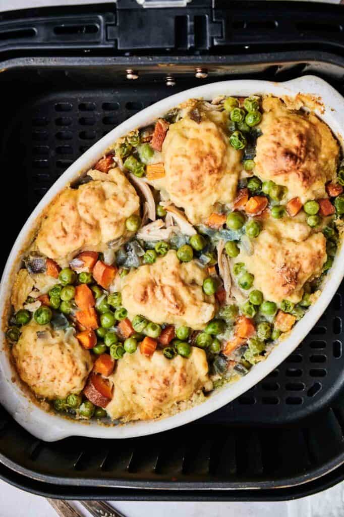 An oval dish of Air Fryer Chicken and Dumpling Casserole, brimming with peas and carrots, sits invitingly in the air fryer.